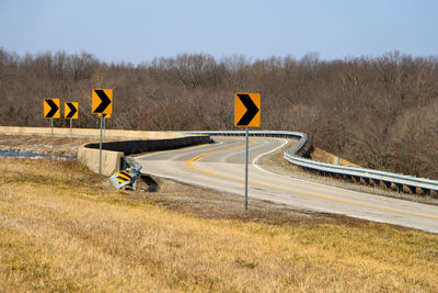 Arrow symbols on empty road against clear sky