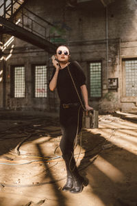 Young woman wearing sunglasses standing against abandoned building