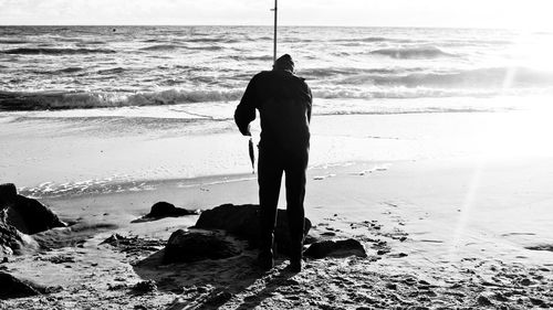 Silhouette man fishing on shore during sunset