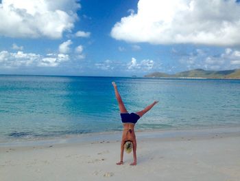 Full length of woman doing handstand at beach against sky