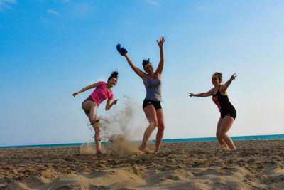 Cheerful friends standing at beach against sky