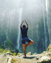 Rear view of woman practicing tree pose against waterfall