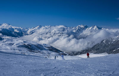 People skiing on snowcapped mountain against clear blue sky