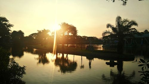 Silhouette trees by lake against sky during sunset