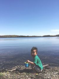 Portrait of boy sitting on lake against clear sky