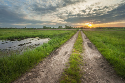 Road amidst field against sky during sunset