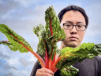 Portrait of man holding plant against sky