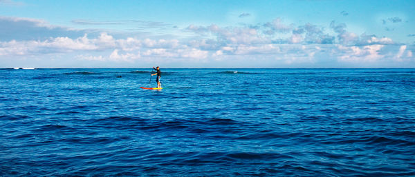 Man paddleboarding on sea against sky during sunny day