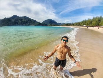 Full length of shirtless man at beach against sky