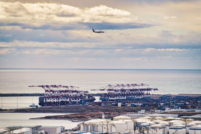 Airplane flying over sea in city against sky