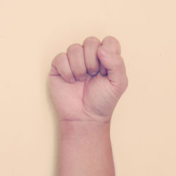 Cropped hand of man clenching fist against beige background