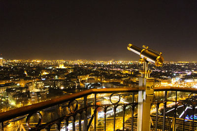 Telescope in balcony against illuminated buildings in city at dusk