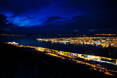 Illuminated cityscape by sea against sky at night