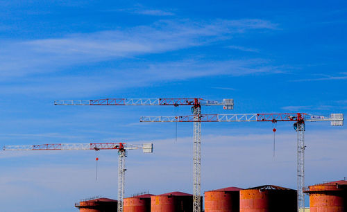 Low angle view of cranes by silo against sky