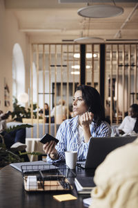 Female entrepreneur talking on smart phone while looking away at coworking office