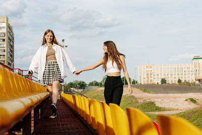 Two teenage girls walk together through the stands of the school stadium, talking, holding hands