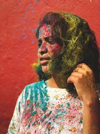 Woman with multi colored powder paint on face against wall during festival