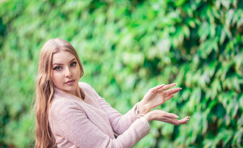 Portrait of young woman gesturing against plants