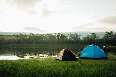 Tent on field by lake against sky