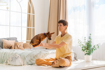 Owner playing with joyful dog at home, happy mature woman enjoying exercise