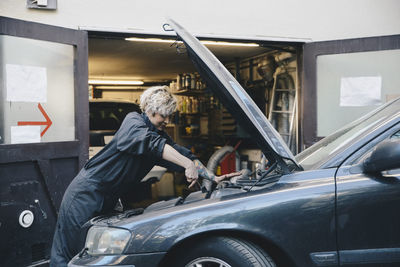 Side view of female mechanic repairing car outside auto repair shop