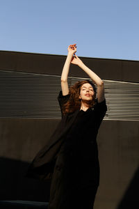 Woman with arms raised standing against wall