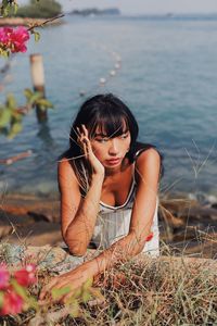 Young woman looking away sitting by sea