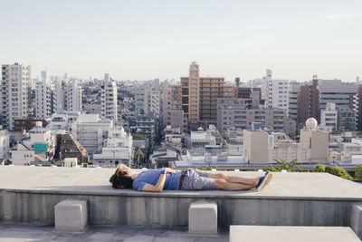 People relaxing by buildings in city against sky