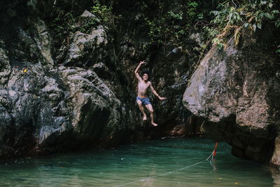 Full length of shirtless young man jumping in river by rock formations