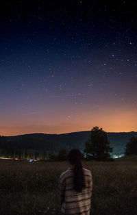 Rear view of woman sitting on field against sky at dusk