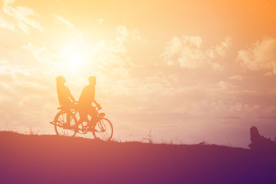 Silhouette people riding bicycle on field against sky during sunset