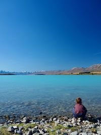 Rear view of man sitting on rock against sea