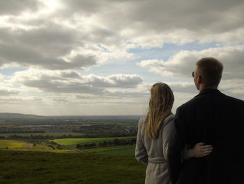 Rear view of man and woman standing on field against cloudy sky