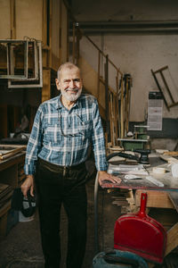 Smiling male carpenter standing near workbench at repair shop