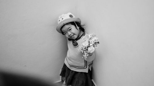 Portrait of smiling girl holding bouquet standing against wall