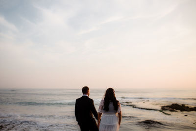 Rear view of couple on beach against sky