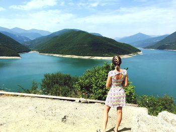 Rear view of woman looking at lake against sky during sunny day