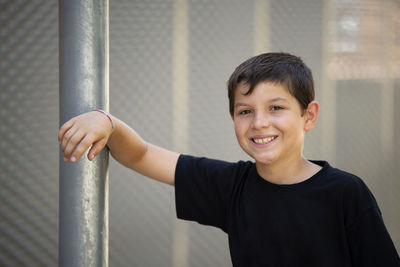Portrait of smiling boy standing by pole