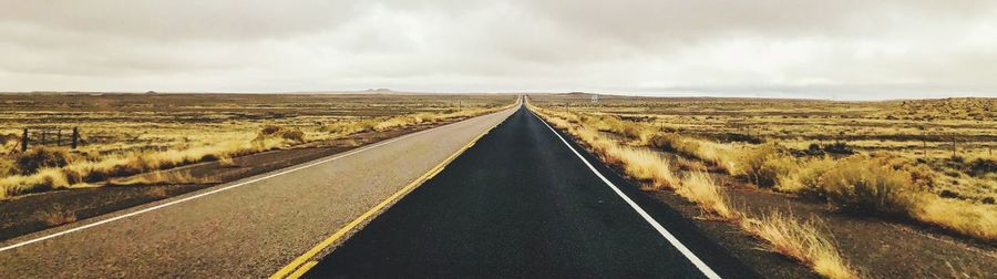 Panoramic view of road amidst field against sky
