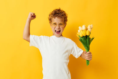 Portrait of smiling boy holding bouquet against yellow background