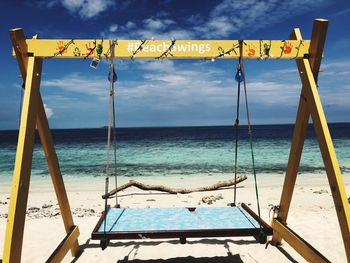 Scenic view of swing at beach against cloudy sky