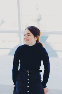 Smiling young woman standing against window