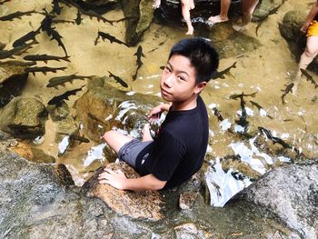 High angle view of boy on rock by pond