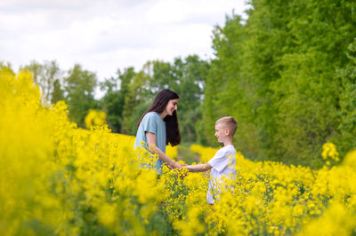 Rear view of woman standing amidst yellow flowering plants on field