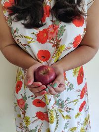 Midsection of woman holding red while standing against white wall