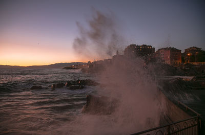 Waves splashing on shore against sky during sunset