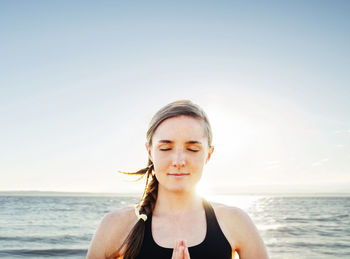 Woman meditating in lotus position by sea against sky