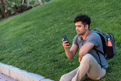 Young latin man sitting in the grass using the mobile phone.