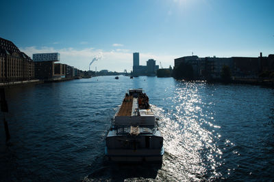 Boat sailing on river in city against blue sky