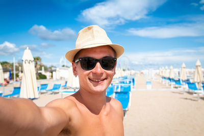 Portrait of shirtless man wearing sunglasses at beach against sky